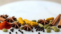 Aromatic spices and herbs scattered on white surface including star anise, cardamom, turmeric, cinnamon, black pepper for culinary cooking and seasoning.