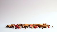 Aromatic spices and herbs scattered on white background including cinnamon sticks, star anise, peppercorns and dried chilies for culinary cooking.