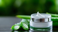 Luxury white cosmetic cream jar with fresh green leaves on dark background, natural organic skincare product for beauty and spa treatments.