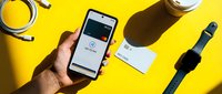 Hand holding smartphone with tap to pay screen, credit card, smartwatch on yellow background, modern contactless payment concept.