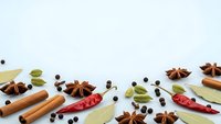 Aromatic spices and herbs scattered on white background including cinnamon sticks, star anise, bay leaves, peppercorns and chili peppers for cooking.