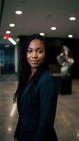 Professional African American businesswoman with braided hair in modern office environment smiling confidently at camera wearing dark business suit.