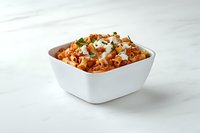 Creamy buffalo chicken pasta salad topped with blue cheese crumbles and fresh herbs in white square bowl on marble surface, ready for serving.