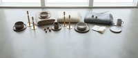 Minimalist dining table setup with brown ceramic plates, cups, brass candlesticks and neutral linens arranged on white surface near window for home decor.