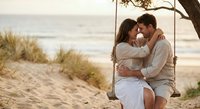 Young couple embracing on wooden swing at sandy beach during golden hour sunset, romantic moment by ocean waves with natural dunes and grass in background.