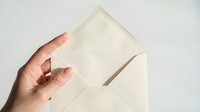 Hand holding open cream envelope with blank card emerging, elegant stationery for invitations, correspondence, and greeting card designs.