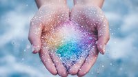 Cupped hands holding magical rainbow glitter and sparkles against soft blue background, symbolizing hope, dreams, and wonder. Dreamy ethereal atmosphere.