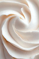 Creamy white meringue or whipped cream swirl in macro close-up showing soft peaks and delicate texture, suitable for bakery and dessert marketing materials.