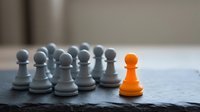 Bright orange pawn standing out among gray pawns on board, representing leadership, uniqueness, and competitive advantage in business strategy and success.