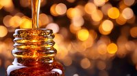 Golden honey pouring into glass jar with warm bokeh background, close up macro shot showing liquid amber sweetness and viscosity in natural light.