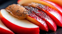 Fresh red apple slices topped with almond butter and black chia seeds on dark background, macro shot of healthy snack preparation.