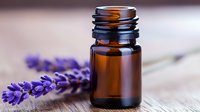 Brown glass essential oil bottle with fresh lavender flowers on wooden surface, soft focus background for aromatherapy and wellness concepts.