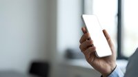 Male hand holding blank white smartphone screen in modern office environment with blurred background for app mockup and digital technology concepts.