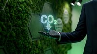 Businessman holding glowing CO2 reduction symbol against green moss wall, representing carbon footprint decrease and sustainable business strategy.