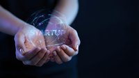 Hands holding glowing digital globe with startup text and network connections on dark background, representing entrepreneurship, innovation, and business growth.