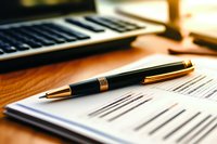 Luxury pen on business contract papers with calculator in background, warm lighting creates professional atmosphere for signing documents and agreements.