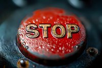 Red metallic button with embossed STOP text captured in extreme macro photography showing water droplets and textured surface detail against dark background.