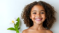 Young African American girl with curly hair and bright smile holding white lily flower against light background, expressing joy and natural beauty.