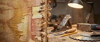 Weathered wooden plank with peeling paint layers in carpentry workshop. Rustic texture for renovation, restoration, crafts projects.