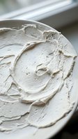 Creamy white frosting or whipped cream with textured swirls and peaks in a bowl, ready for cake decorating, baking projects, or culinary applications.