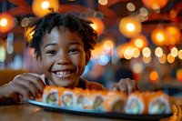 Young African American girl smiling brightly at sushi restaurant with bokeh lights in background, expressing joy and excitement over plate of fresh maki rolls.