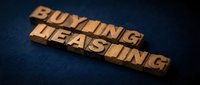 Wooden block letters spelling "buying leasing" on dark blue textured surface, representing real estate and property rental business concepts.