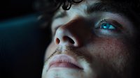 Close up portrait of young caucasian male with freckles and intense blue eyes looking up in dramatic moody lighting, showing contemplative expression.