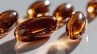 Amber-colored translucent gel capsules with soft shadows and light reflections on white surface, macro photography showing medical supplement pills in warm tones.