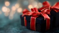 Navy blue gift box wrapped with red satin ribbon and bow against dark background with soft bokeh lights creating festive holiday atmosphere.