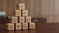 Wooden blocks stacked in pyramid formation with engraved symbols representing business growth, strategy, and financial success for corporate planning and organizational development.