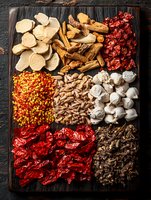 Assorted Chinese dried herbs, mushrooms and spices arranged on dark wooden board. Traditional Asian cooking ingredients displayed in organized sections.