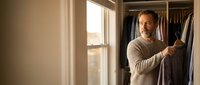Middle-aged Caucasian man organizing clothes in walk-in closet, selecting shirt from wardrobe. Morning routine, lifestyle concept for home organization.