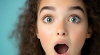 Close up portrait of young woman with curly hair expressing surprise and amazement with wide open mouth and eyes against turquoise background.