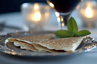 Thin crispy crepes served on ornate silver plate with fresh mint garnish, romantic candlelit setting creates warm ambiance for elegant dessert presentation.
