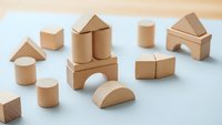 Natural wooden building blocks set with geometric shapes including triangles, cylinders, cubes and arches arranged on white surface for educational play.