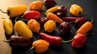 Colorful assortment of fresh hot chili peppers in various shapes and sizes including yellow, red, orange varieties scattered on dark surface for cooking.