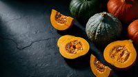 Fresh autumn pumpkins and squash varieties with orange flesh displayed on dark slate surface for seasonal cooking and harvest recipes.