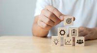 Business person arranging wooden blocks with strategy icons including target, lightbulb, growth chart, and teamwork symbols on desk for planning.