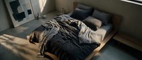 Man sleeping on bed with messy blankets and pillows in minimalist bedroom with natural sunlight, conveying rest and relaxation for lifestyle and wellness content.