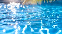Sparkling blue swimming pool water surface with sunlight reflections creating bright bokeh effect and ripple patterns. Refreshing summer background.