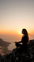 Young woman practicing meditation yoga on mountain cliff overlooking ocean during golden hour sunrise for mindfulness wellness and spiritual peace.
