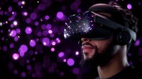 Young bearded African American man wearing VR headset with purple bokeh lights reflecting in lenses, experiencing virtual reality against dark background.