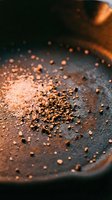 Toasted coriander seeds scattered in cast iron skillet with warm lighting, suitable for culinary, food styling, and cooking content.