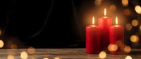 Red candles burning with warm flames on wooden surface creating cozy atmosphere with golden bokeh lights in dark background for holiday decoration.