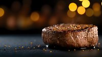 Juicy grilled beef steak with spices and seasonings on dark background with golden bokeh lights. Close up view of medium rare tenderloin filet mignon.