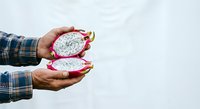 Hands holding halved dragon fruit with white flesh and black seeds against white background, suitable for food and nutrition content.