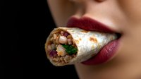 Sensual close up of red lips holding fresh shawarma wrap with grilled meat, vegetables and sauce. Middle Eastern street food concept for menu design.