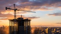 Construction crane building residential tower at sunset with dramatic sky and city skyline in background for urban development projects.