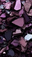 Crushed purple and plum eyeshadow pieces with metallic shimmer texture creating abstract pattern of broken cosmetic powder fragments in dark moody lighting.