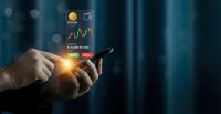 Businessman hands holding smartphone with glowing financial trading chart and cryptocurrency icons floating above screen in modern office environment.